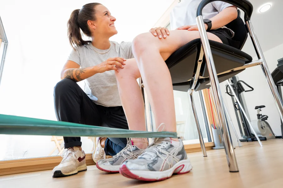 Patientin trainiert unter Anleitung der Physiotherapeutin mit dem Theraband im Übungsraum