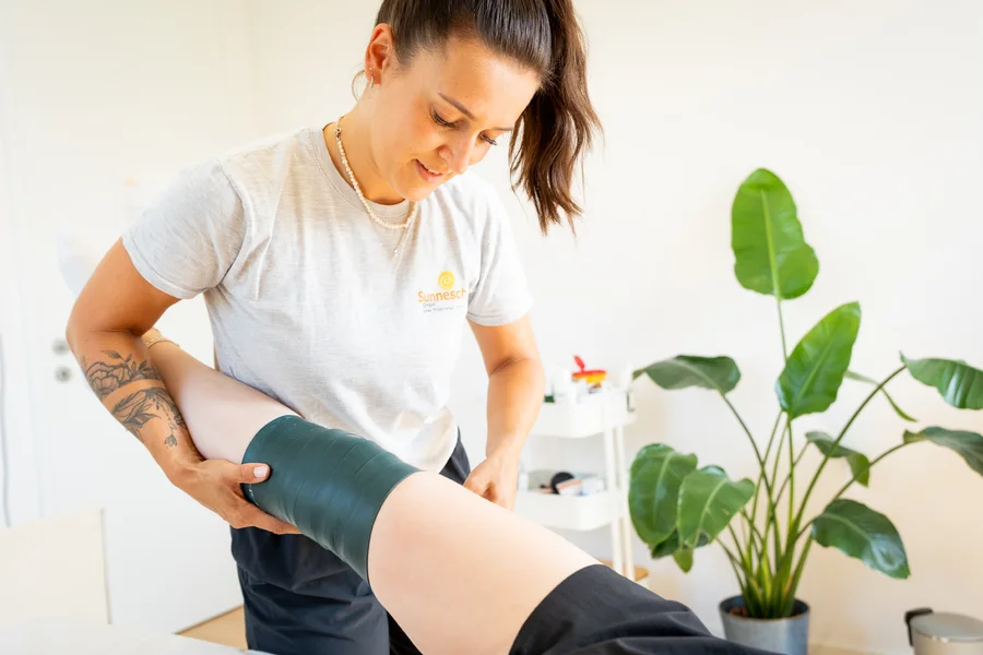 Physiotherapeutin legt ein Kompressionsband (Flossing) am Knie einer Patientin an.