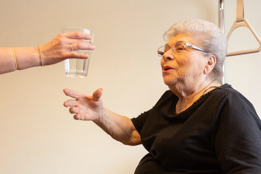 Pflegefachperson reicht einer älteren Frau ein Glas Wasser zur Medikamenteneinnahme