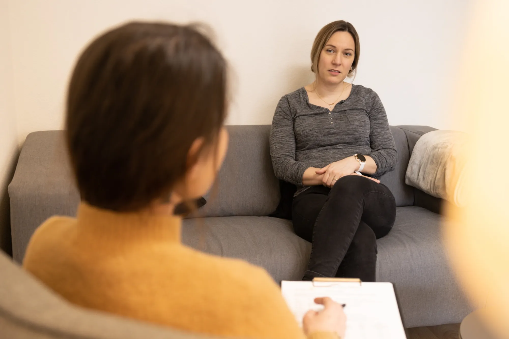 Fachperson der Psychiatrie Spitex sitzt einer jüngeren Person in einem ruhigen, hellen Wohnzimmer gegenüber, offenes, aufmerksames Gespräch, keine klinische Ausstattung, natürliches Licht
